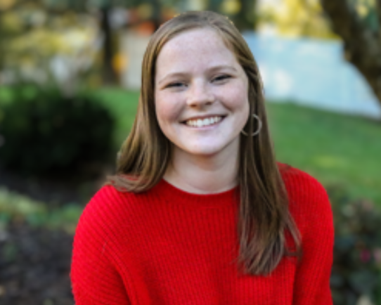 Young woman in a red sweater smiling as she looks at the camera.